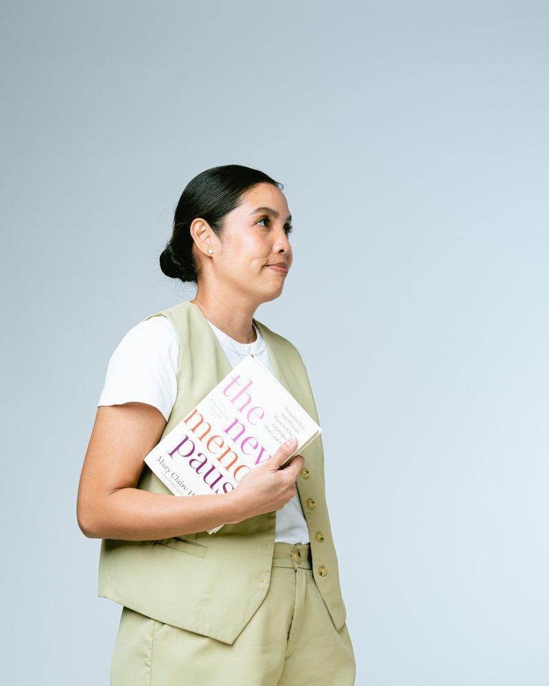 A woman standing with a book about menopause, looking up