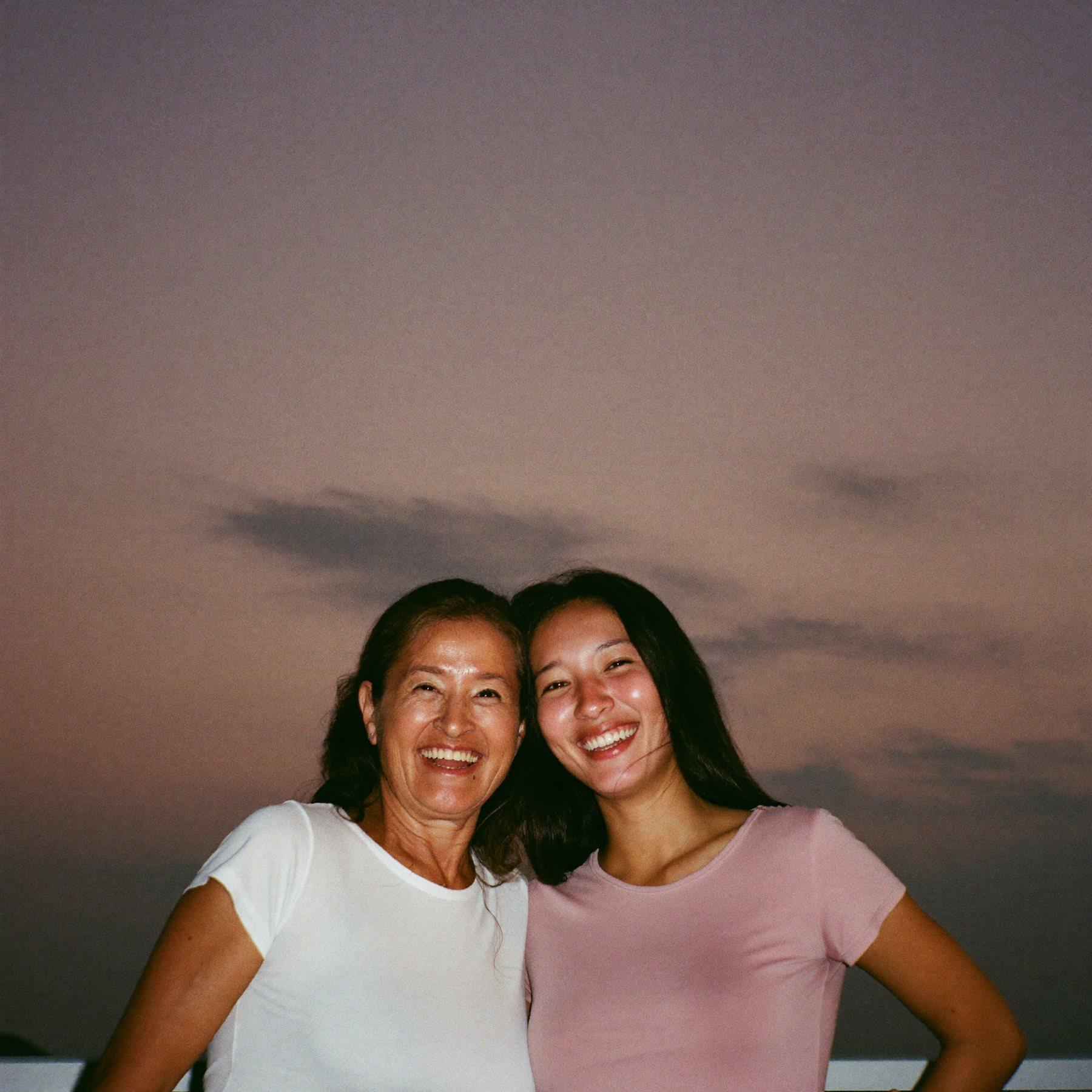 A mother and her grown daughter laughing together at dusk